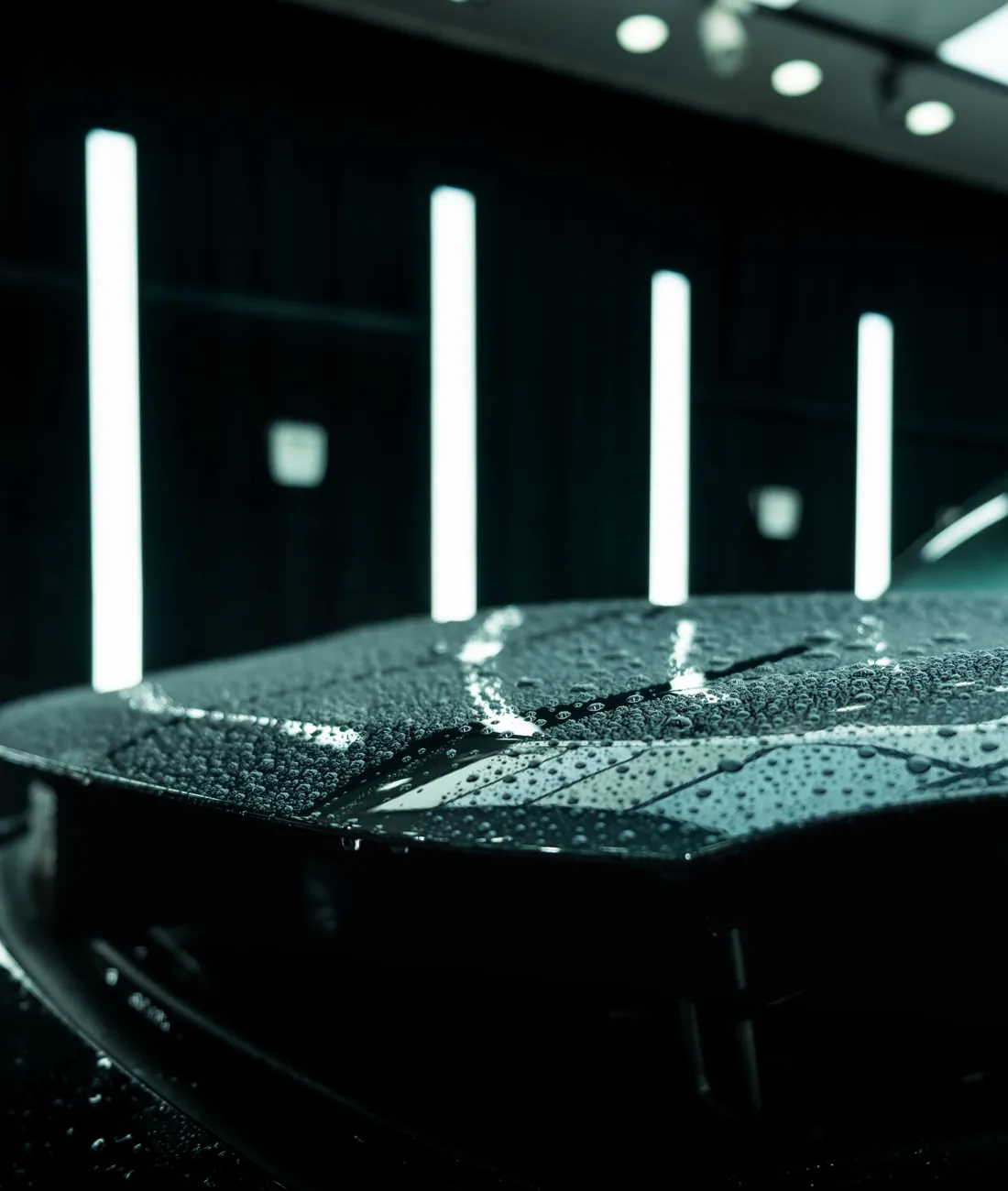Freshly coated black car with water beading on the hood under detailing studio LED light bars