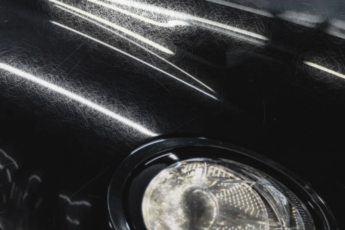 Glossy black fender before correction, hazy with swirl marks around the light reflections